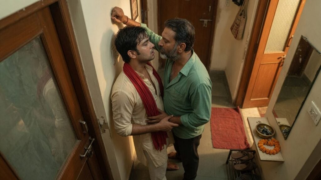 Two fully clothed adults, one adult Indian man and one adult Indian man in an Indian apartment entry.