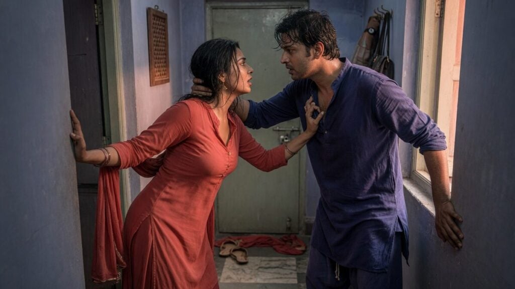 Two fully clothed adults, one adult Indian woman and one adult Indian man in an Indian apartment entry.
